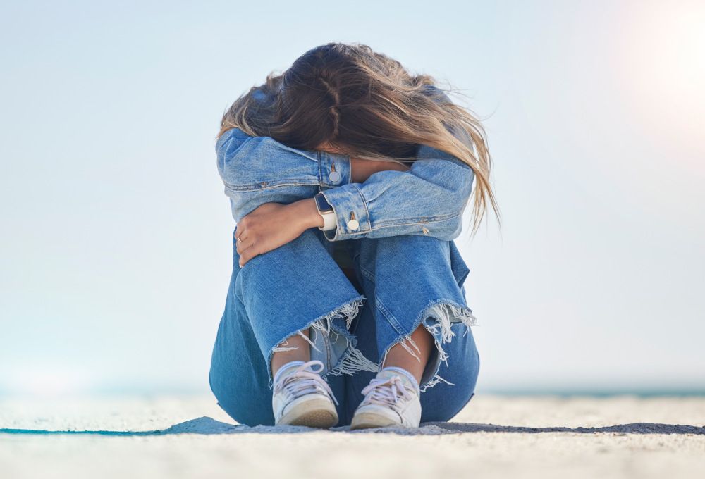 Una chica triste sentada en el suelo con la cabeza entre las piernas. Concepto de gestión de emociones.